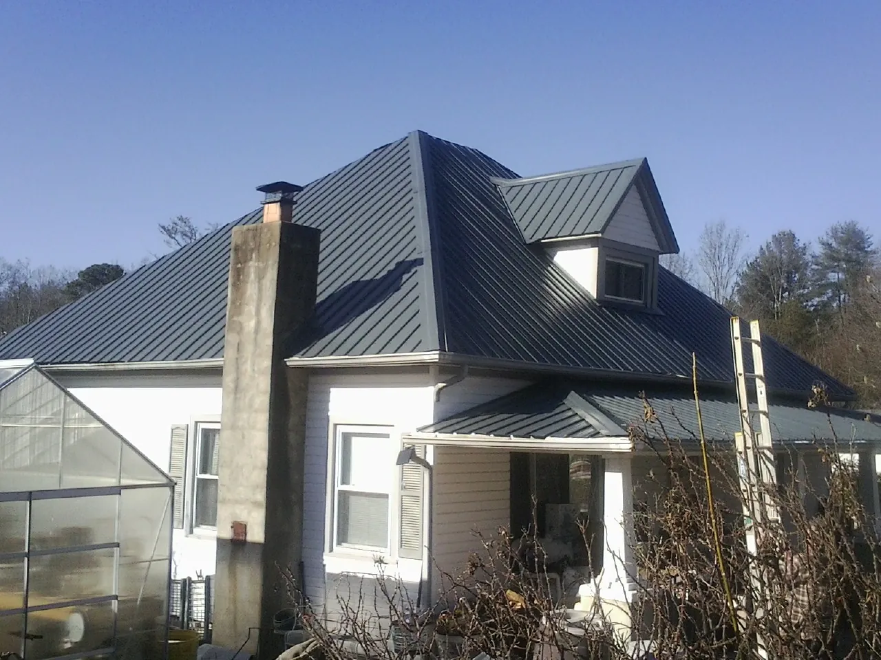 Dark blue standing seam metal roof on a white farmhouse with dormer — Slate & Tile Roof Repair by Roofing Brothers in Verbena