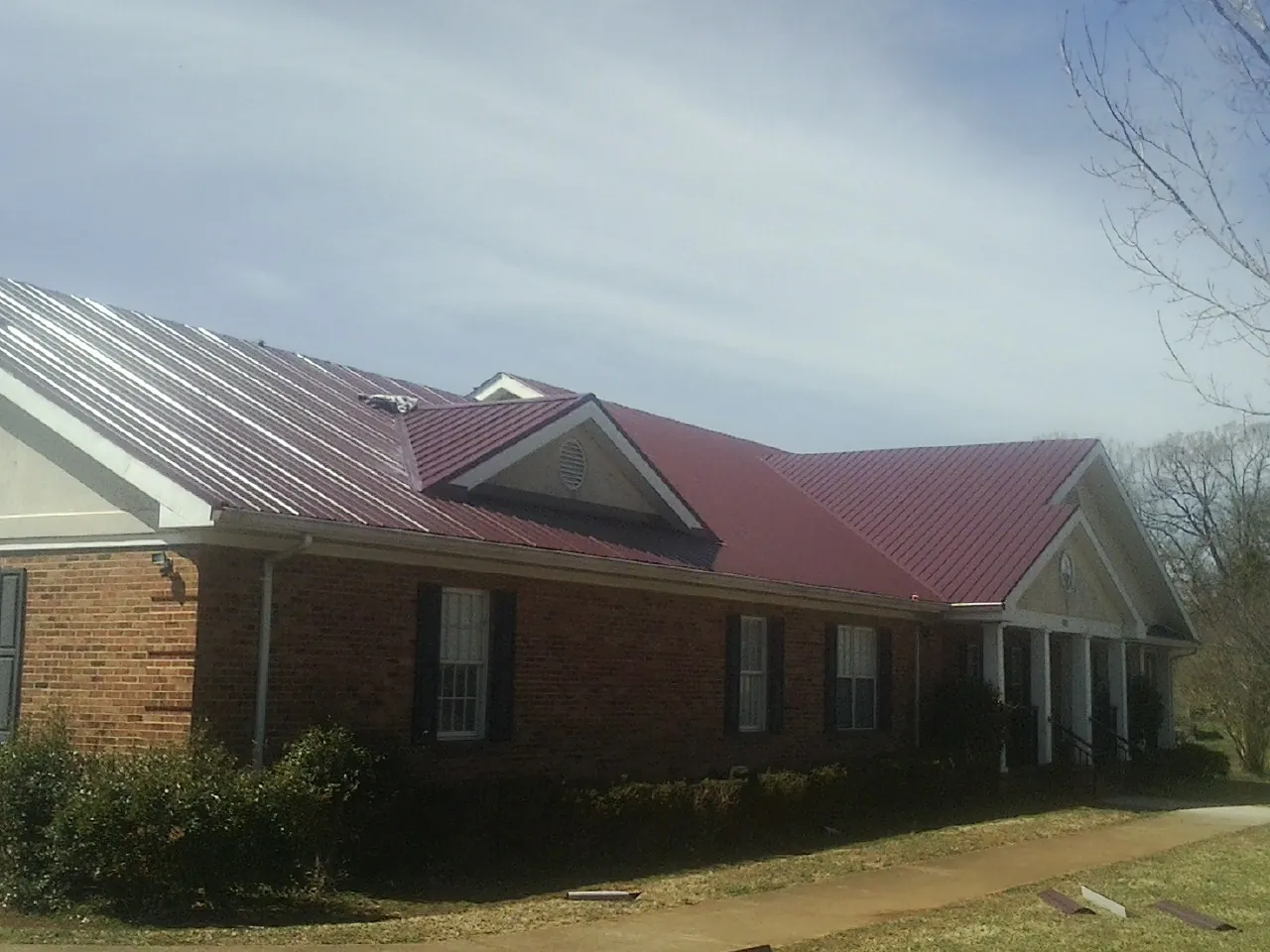 Red metal roof with gabled entries on a long brick building, from a Hail Damage Roof Repair job in Verbena
