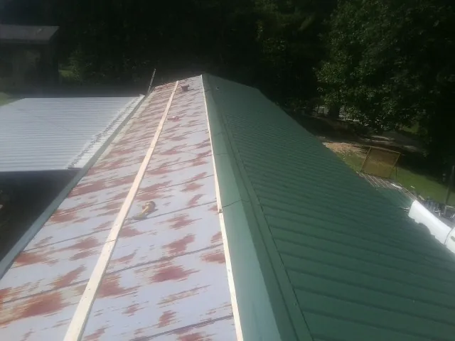 Old rusted panels beside newly installed green metal roofing — Wind Damage Roof Repair by Roofing Brothers in Verbena
