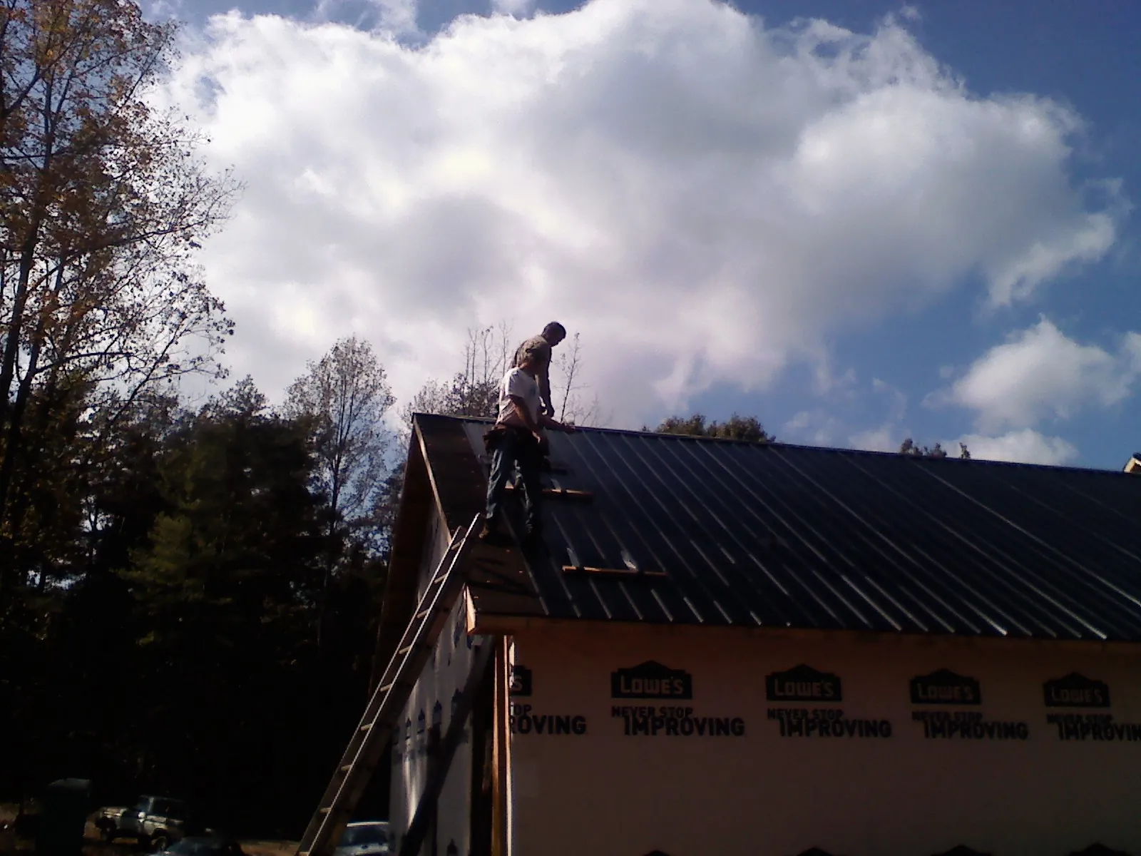 Roofer fastening dark metal panels high against a cloudy sky, from a Roof Inspection job in Verbena