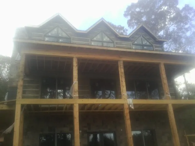 Dormers and porch framing on a large log home under construction — Roof Coating work by our crew in Verbena
