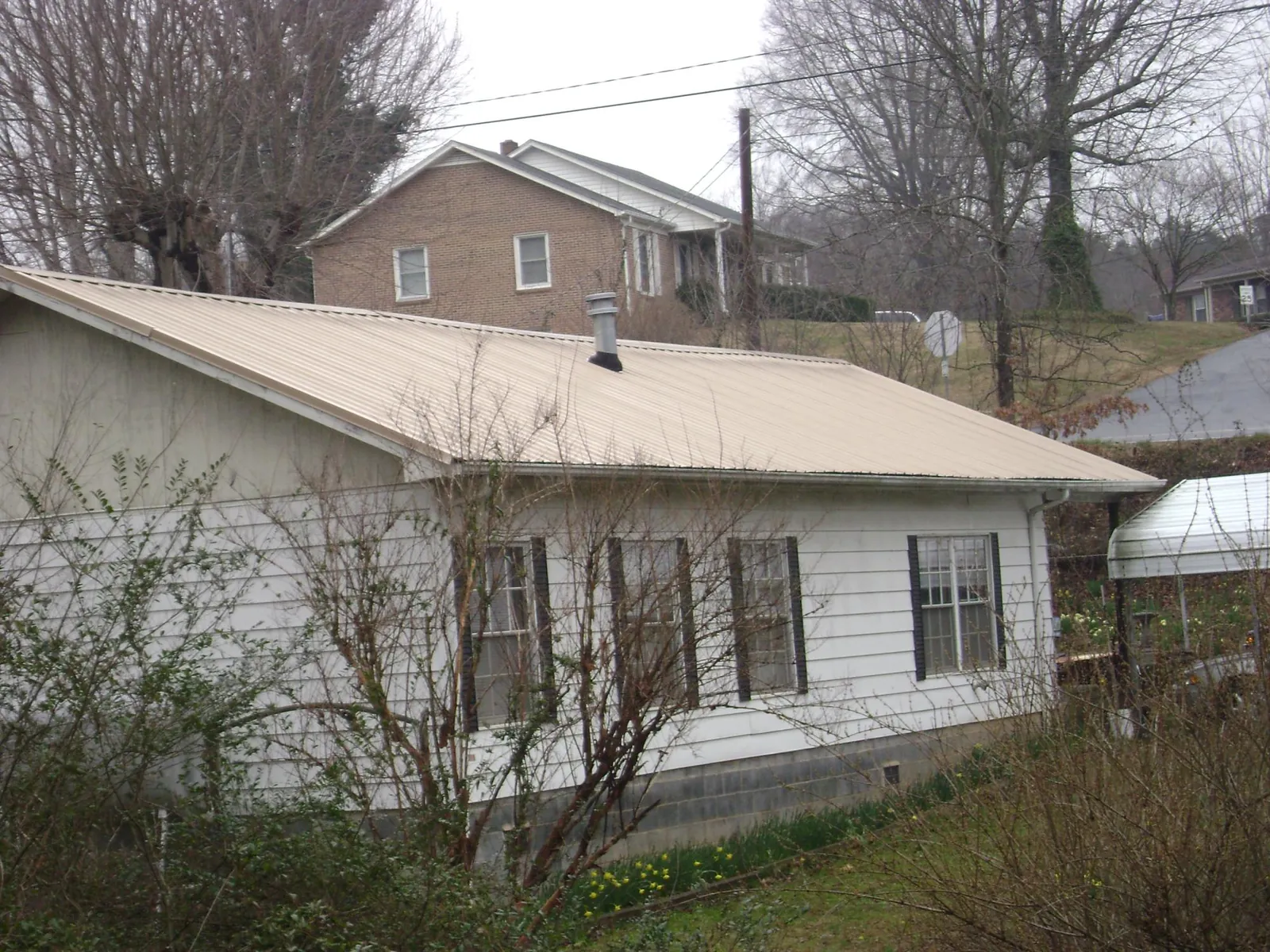 Tan metal roof on a white sided house set into a hillside — Commercial Roofing by Roofing Brothers in Verbena